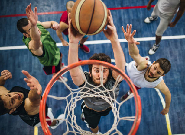 High angle view of a determined basketball player slam dunking the ball while passing through defensive players.